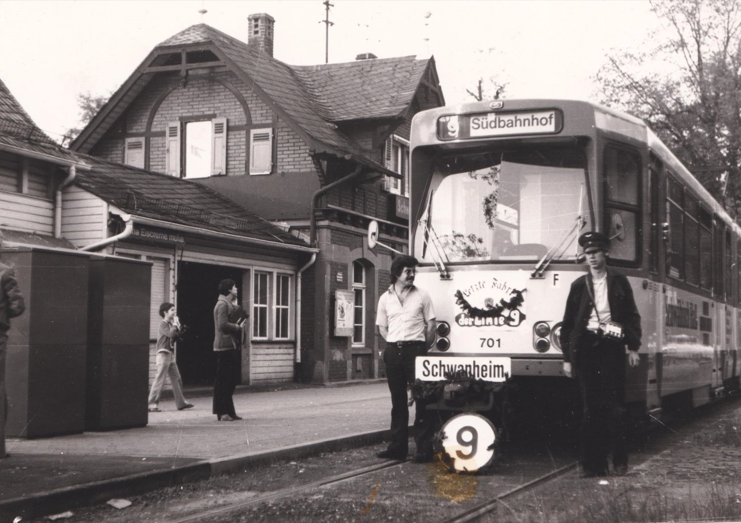 Ein Straßenbahnwagen der Linie 9 mit dem Zielschild „Südbahnhof“ steht an
                      der Endstation Schwanheim. An der Front hängen ein Kranz und ein Schild
                      „Letzte Fahrt der Linie 9“; daneben stehen zwei Männer.