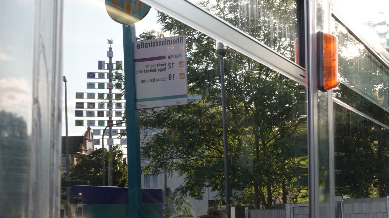 In der Scheibe einer Straßenbahn spiegeln sich der Wappenbaum der
                      Schwanheimer Vereine und das Haltestellenschild „Rheinlandstraße“ mit den
                      Linien 12 und 19; die Schrift erscheint dadurch seitenverkehrt.